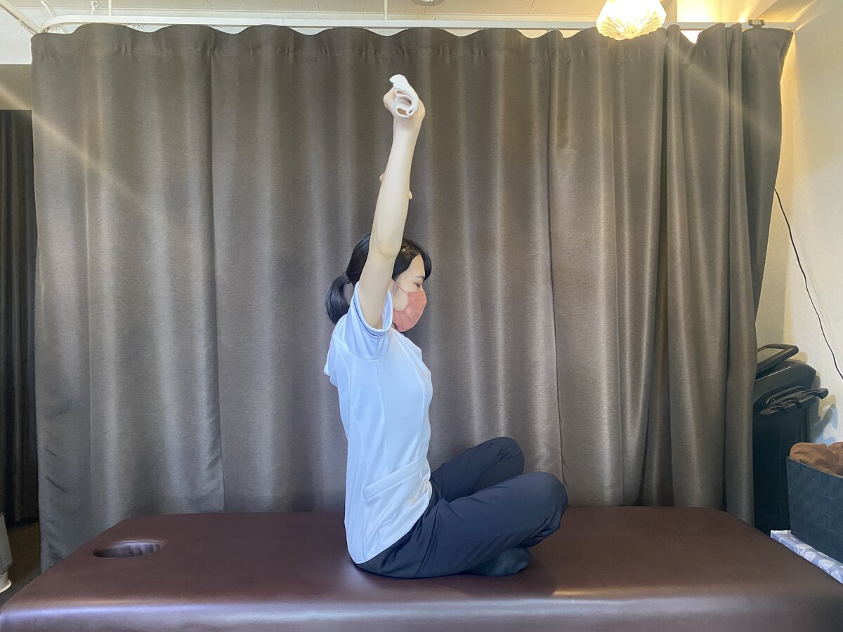 タオルを頭上に持ち上げて肩と胸を伸ばすストレッチ