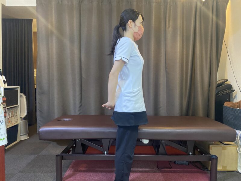 立った姿勢で両手を背中側に合わせ、腕を低い位置で後ろへ伸ばす胸のストレッチ